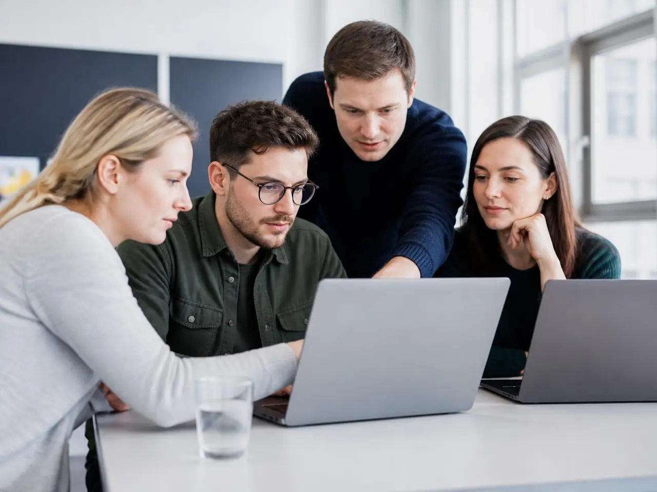 Quatre apprenants travaillent ensemble sur des ordinateurs portables lors d'un atelier pratique.
